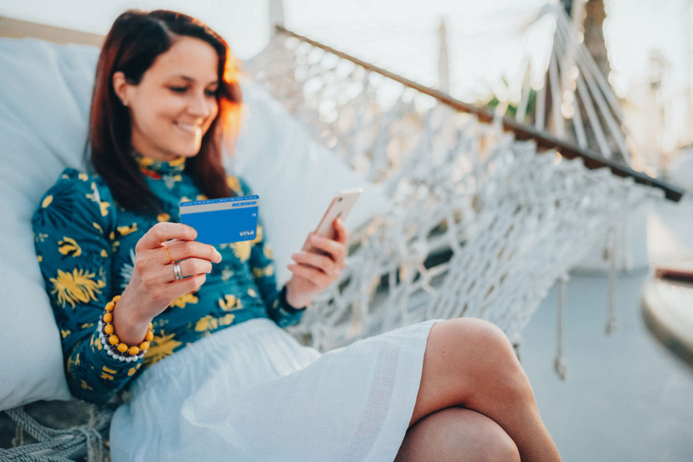 Woman on hammock holding phone and credit card.