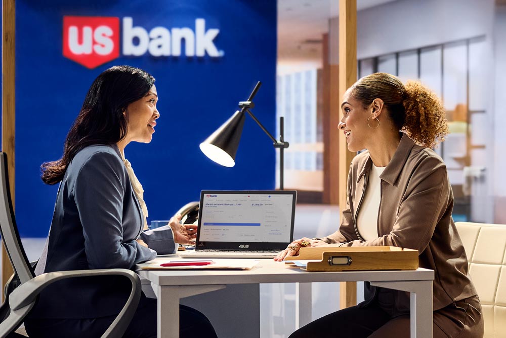 Photo of Jess Sims talking with a banker with Valzure Private Bank sign in background.