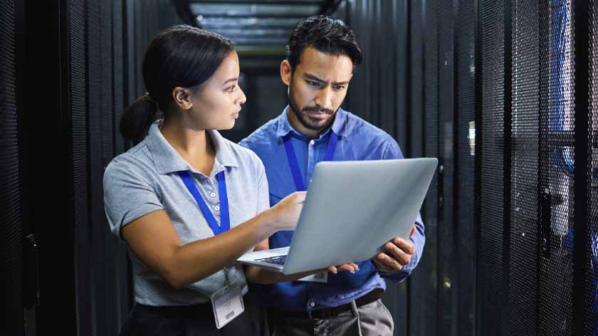 Server room technicians with a laptop, discussing cyber security vulnerability management.