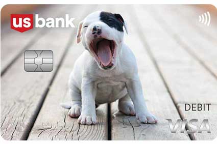 Yawning white puppy with black around eye and ear sitting on wood deck