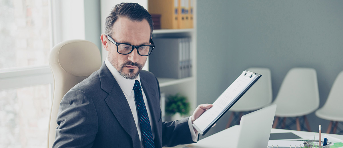 Man in a suit holding a clipboard while at his desk
